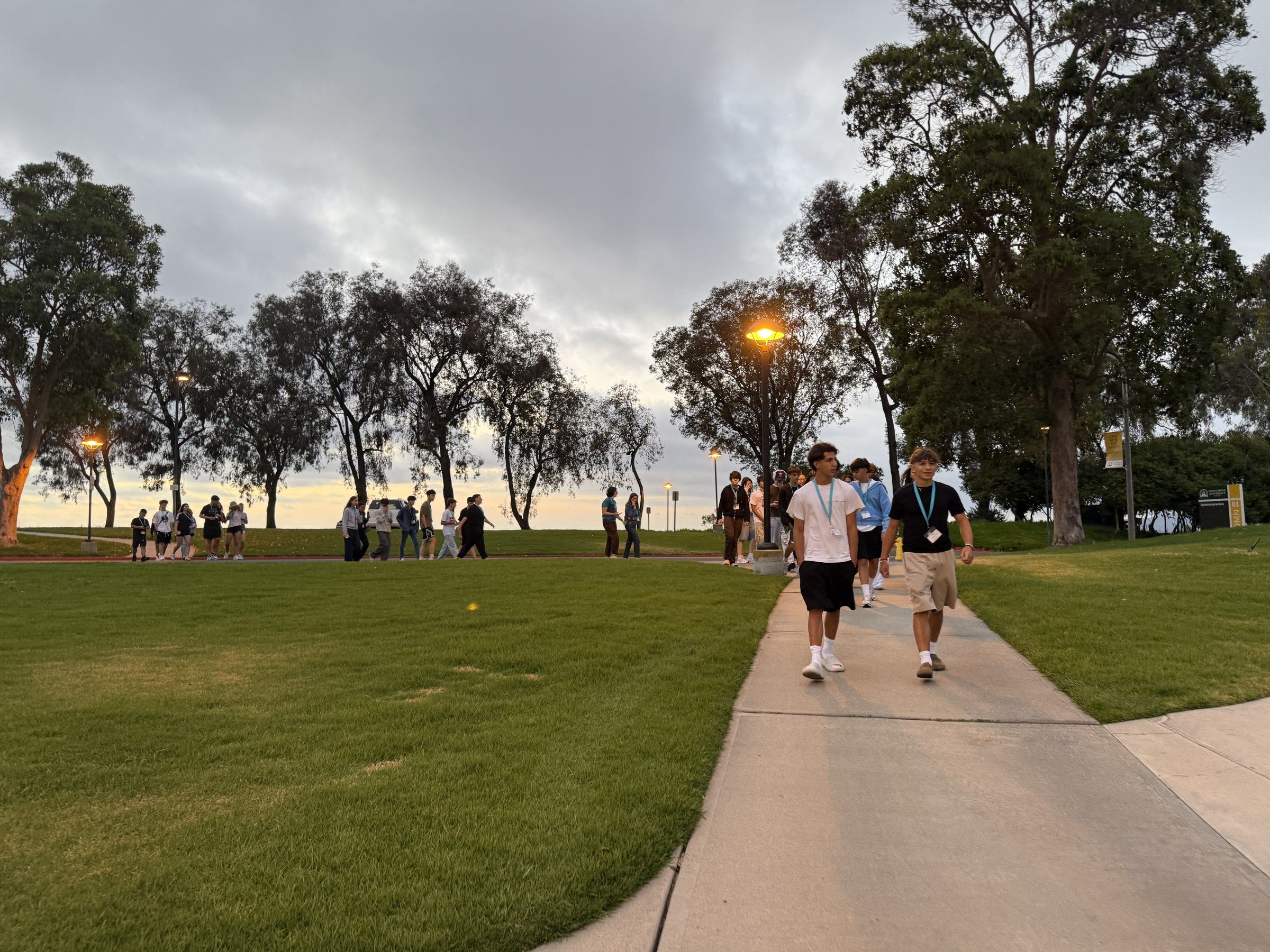 Students walking along a campus path past a lawn at sunset