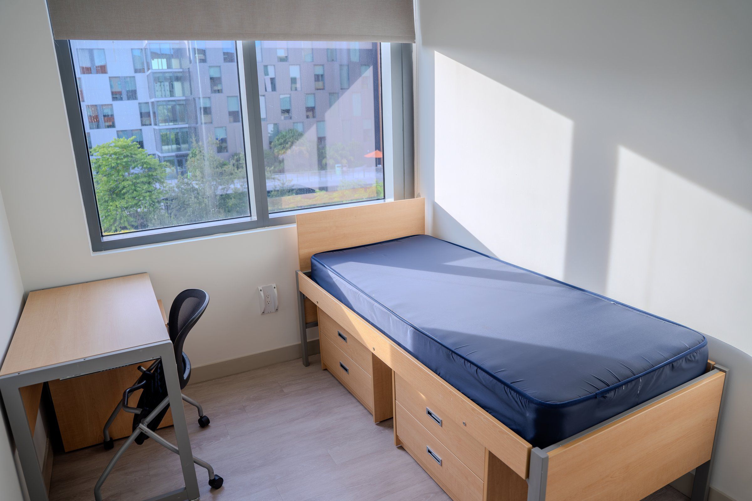 Bed with storage drawers and a desk by the window in a University of Miami residence room