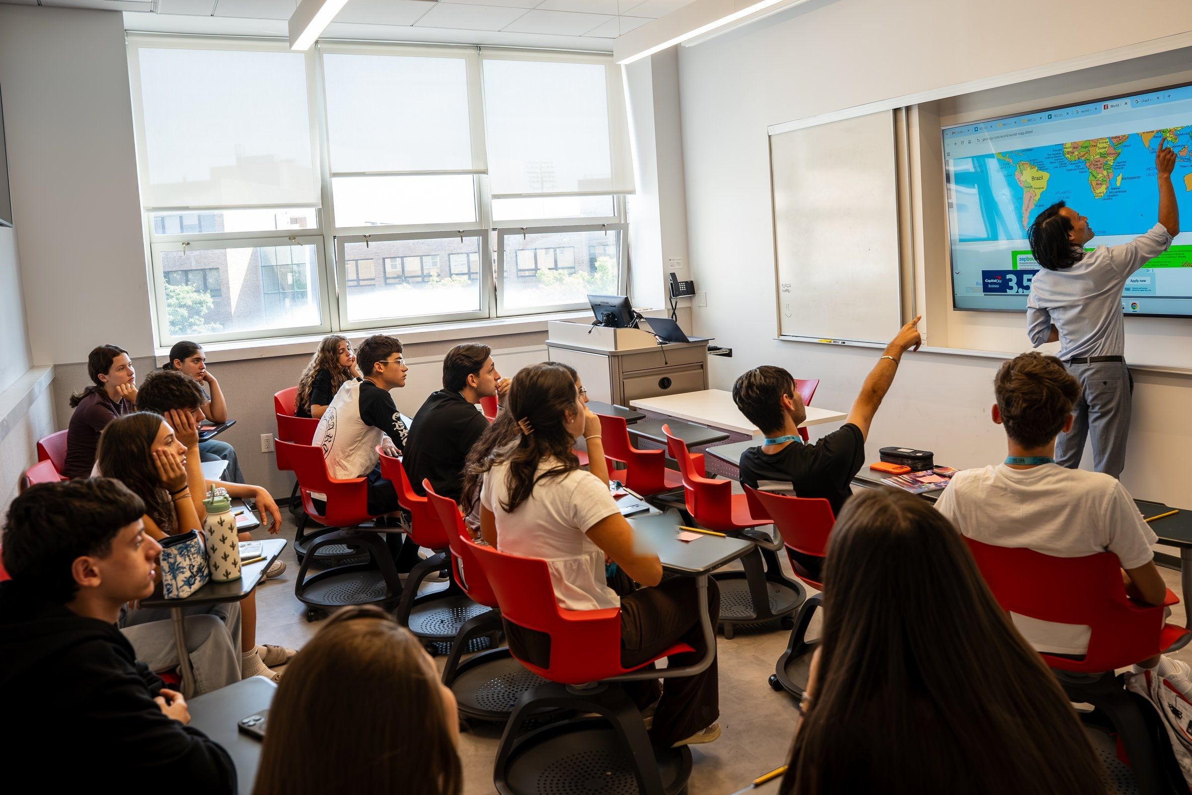 A teacher points to a world map on the screen as YES USA students follow along and one raises a hand, at St. John's University