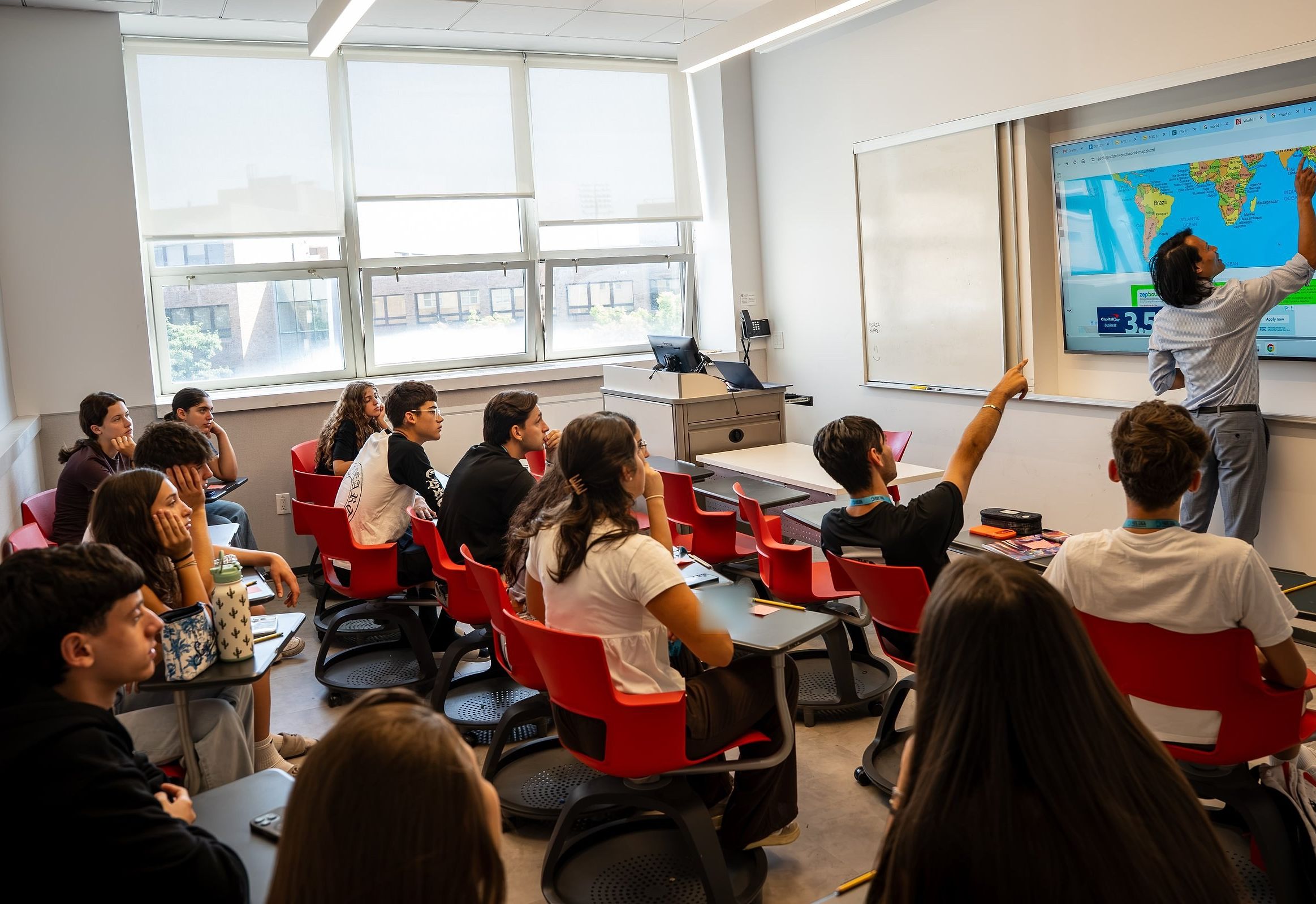 A teacher points to a world map on the screen as YES USA students follow along and one raises a hand, at St. John's University