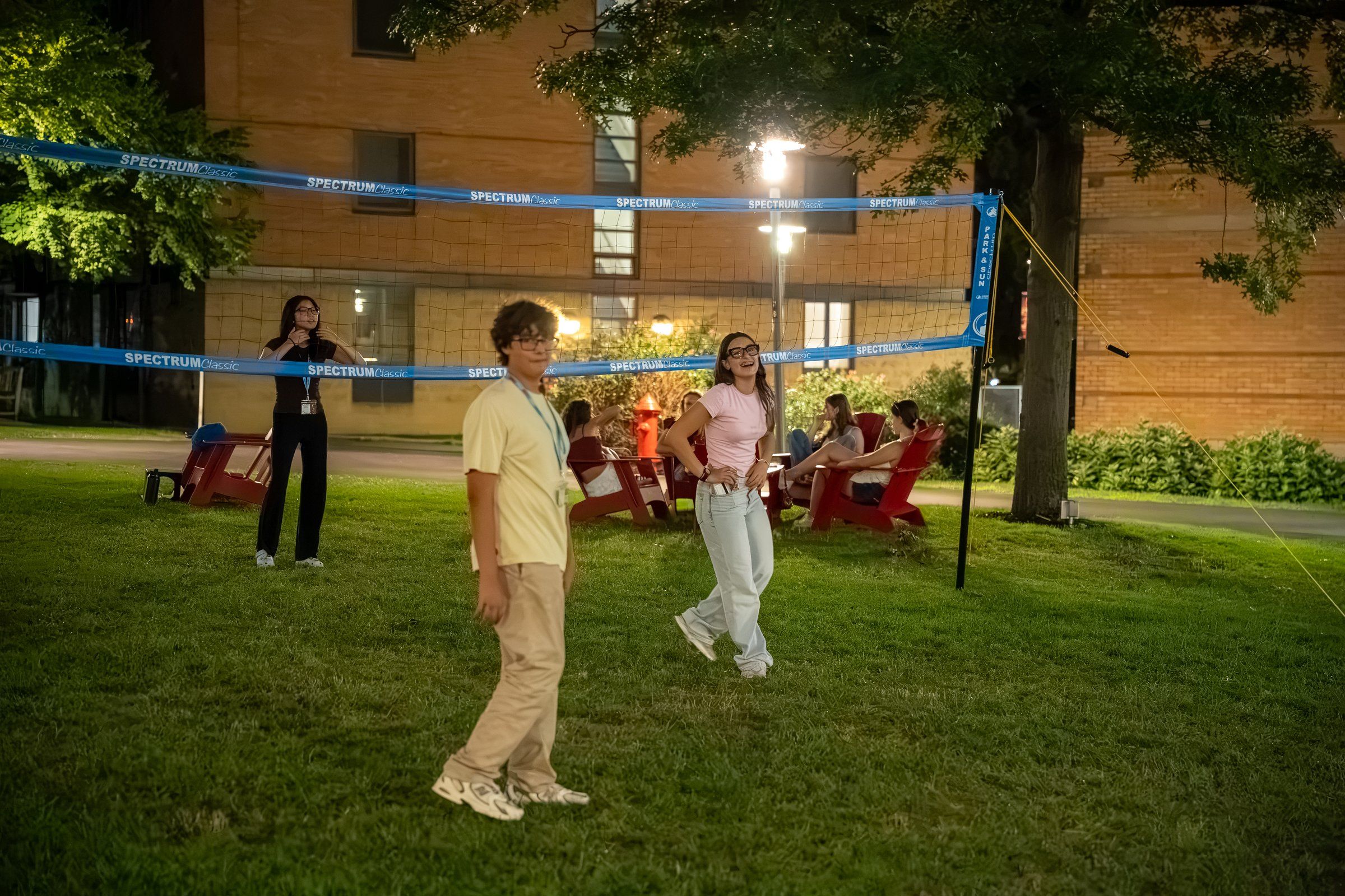 Students playing lawn volleyball outside a residence hall at dusk