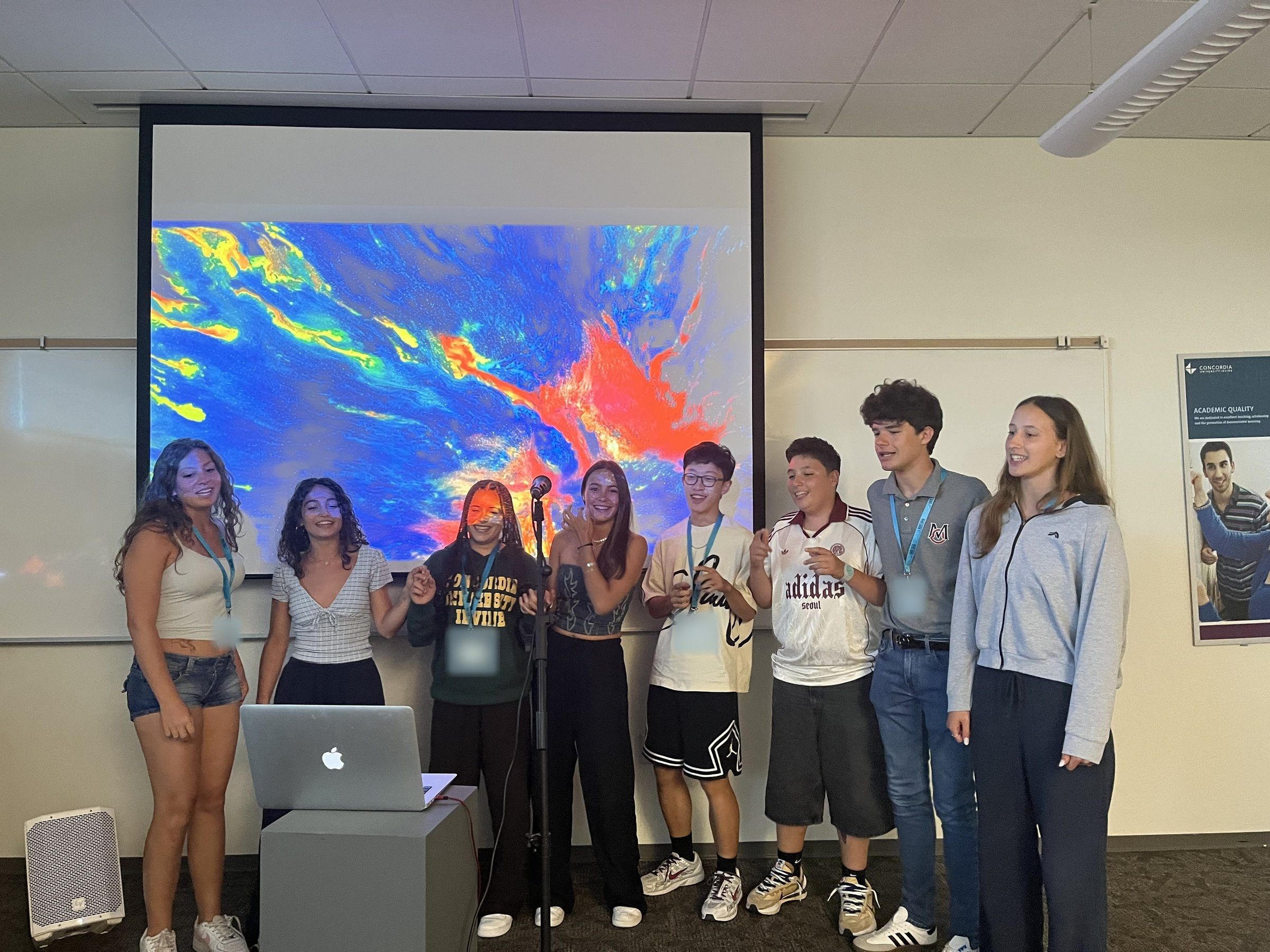 Smiling YES USA students presenting together at a microphone in a Concordia University Irvine classroom