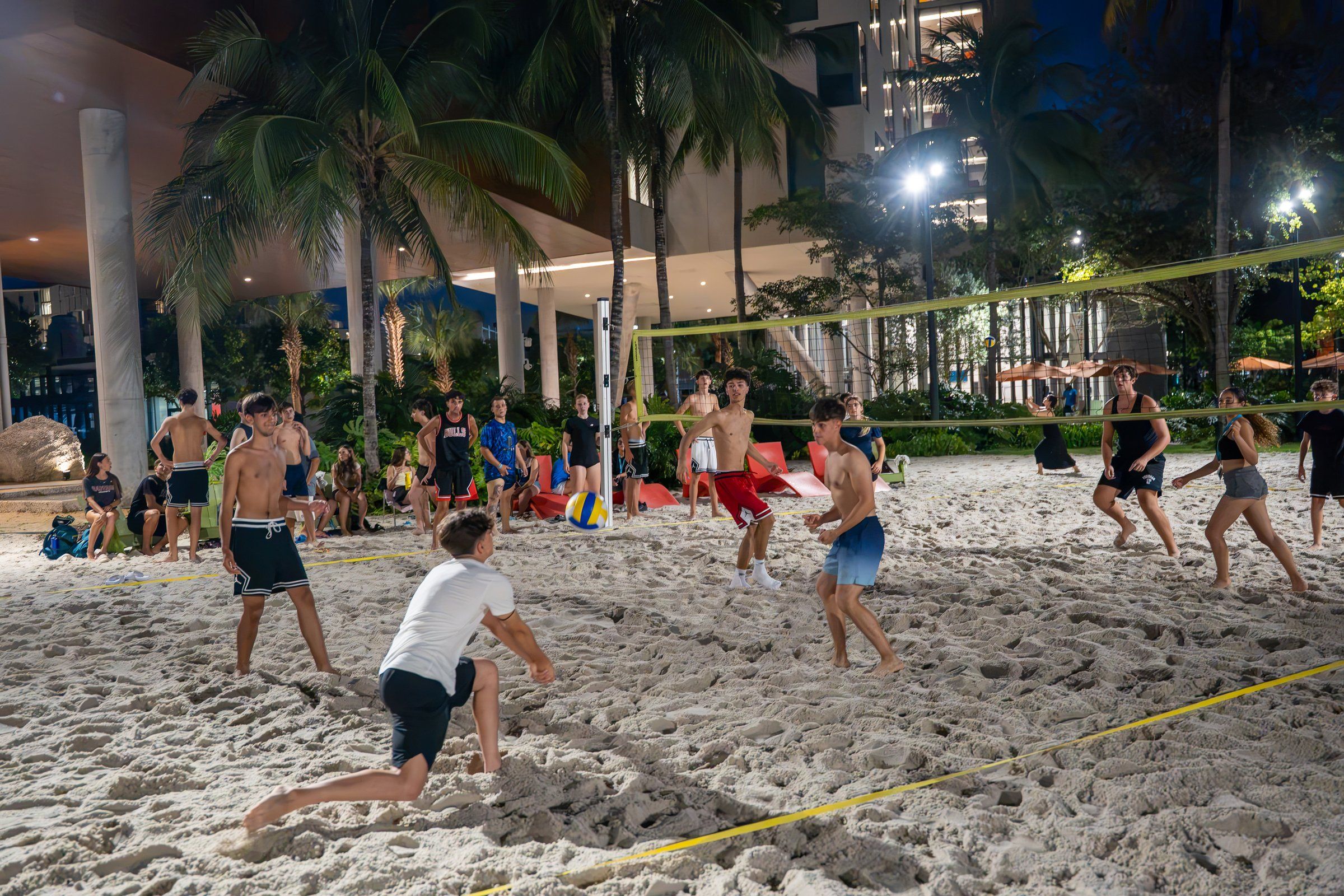 Students playing beach volleyball at night on the floodlit campus sand court