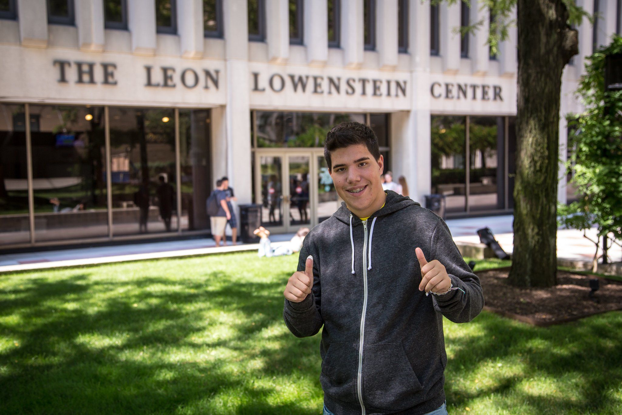 A student giving two thumbs-up on the lawn in front of the Leon Lowenstein Center