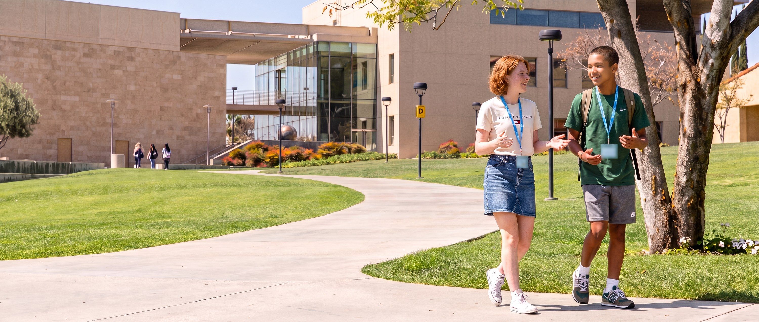 Two students with YES USA lanyards walking and chatting on a campus path at Concordia University Irvine