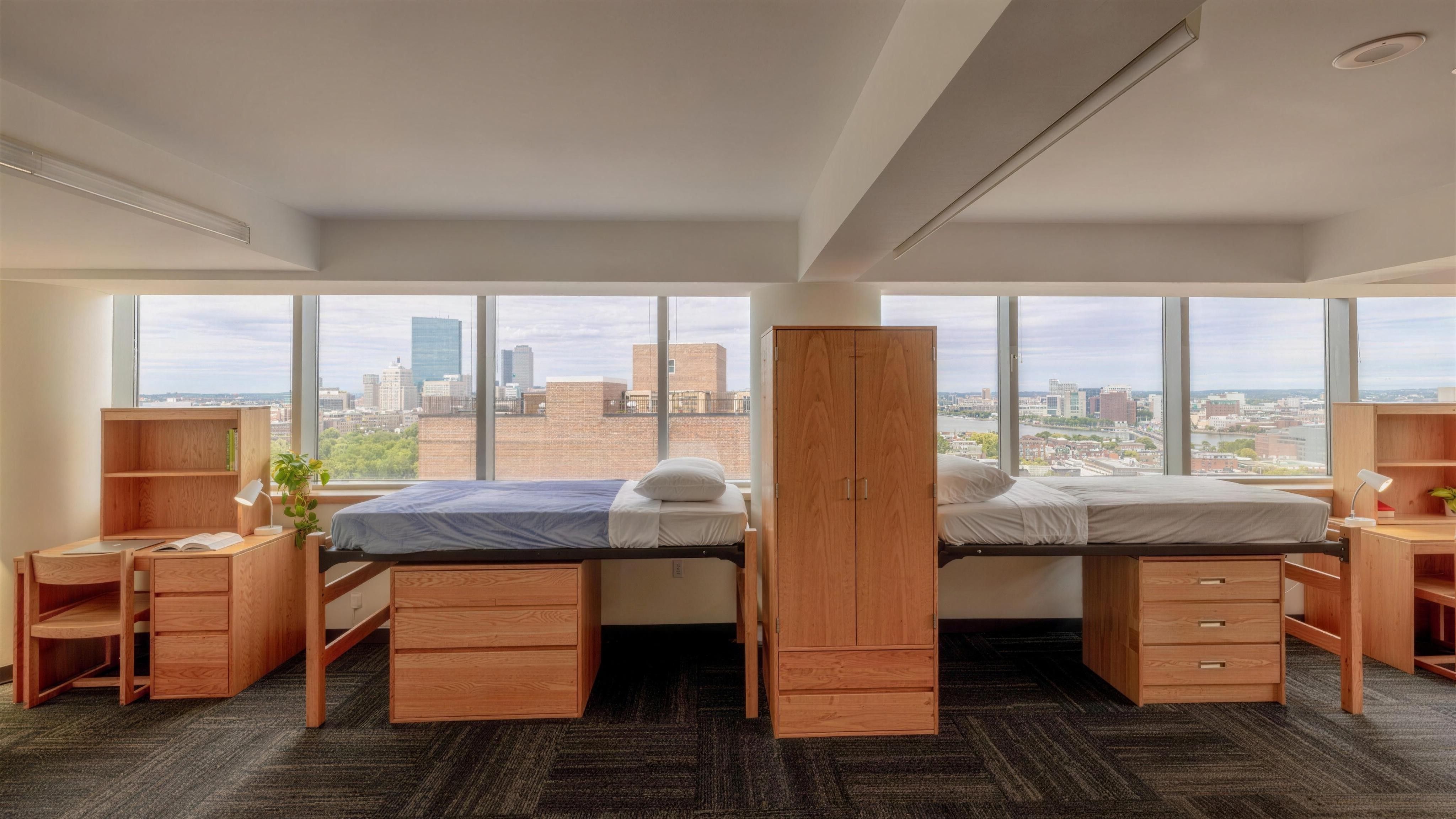 Two beds, desks and a wardrobe in front of floor-to-ceiling windows with a city view in a Miller Hall room