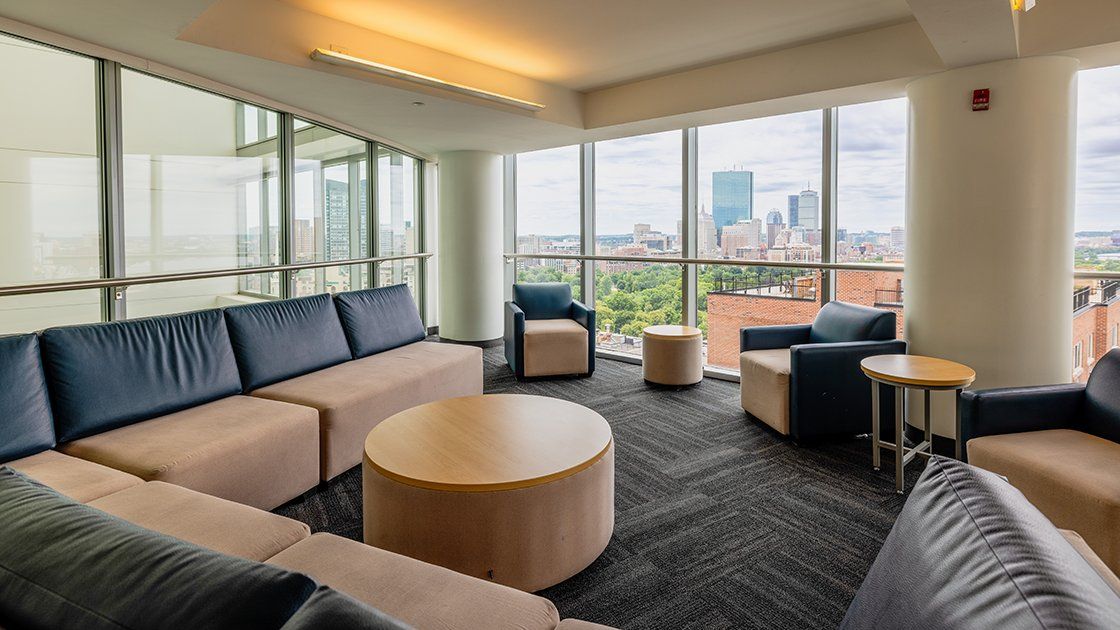 Lounge with sofas and armchairs beside floor-to-ceiling windows overlooking Boston in Miller Hall