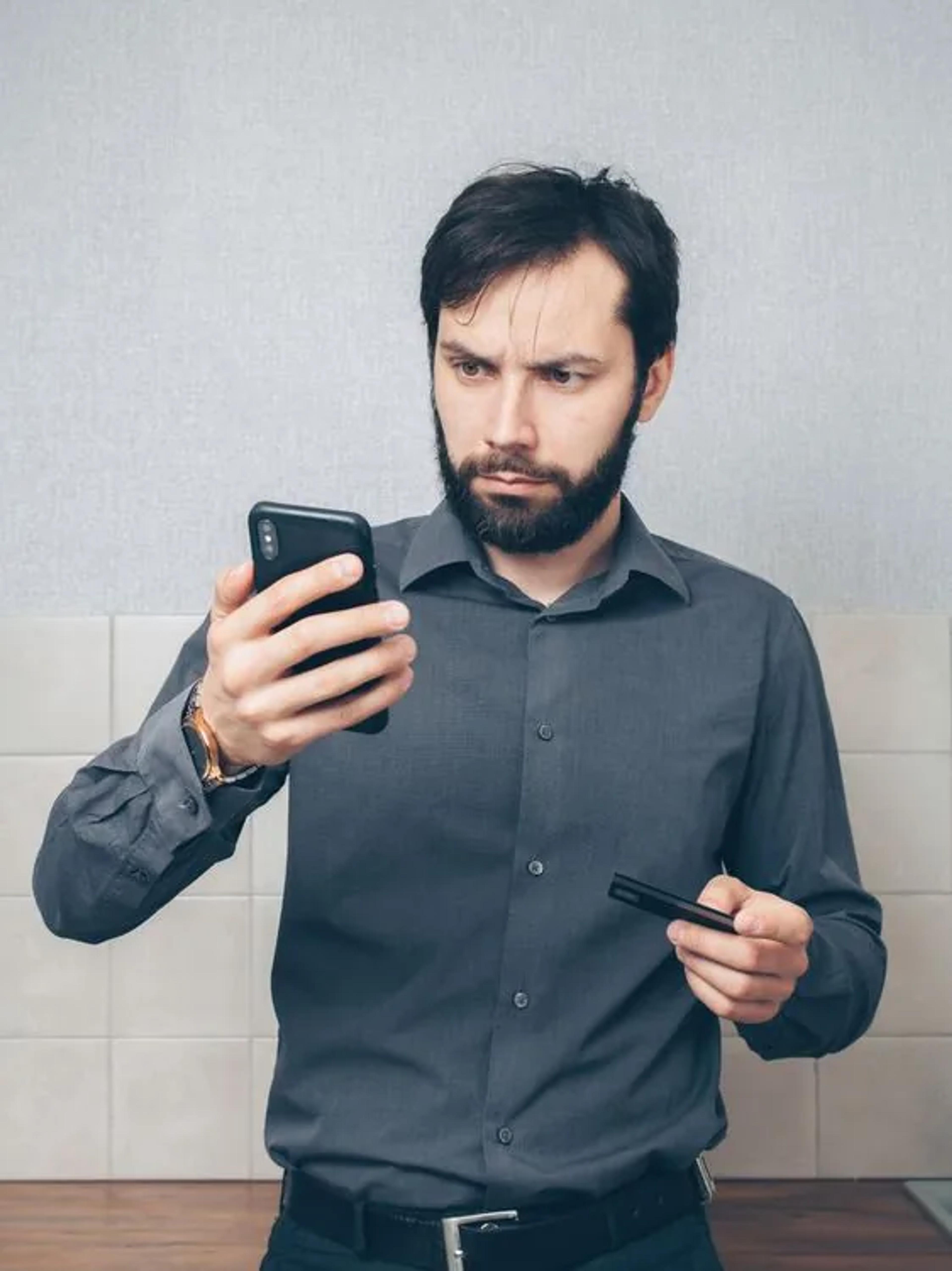 Mann ser på mobiltelefonen mens han holder et betalingskort.