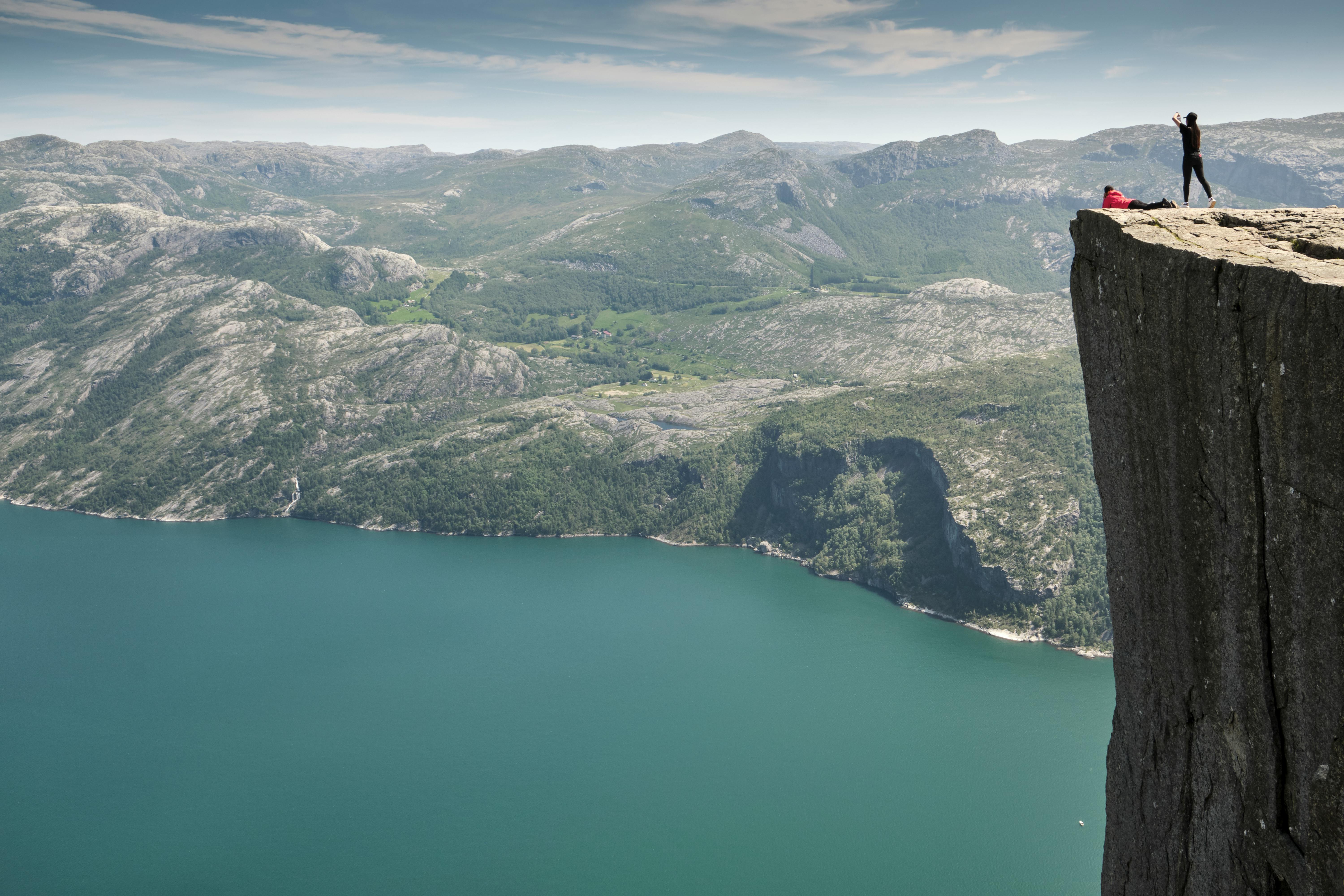Bilde fra preikestolen i Norge. 2 personer som ligger der.