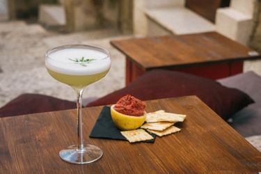 Cocktail on a table with a serving of homemade beetroot hummus served in a used lemon husk