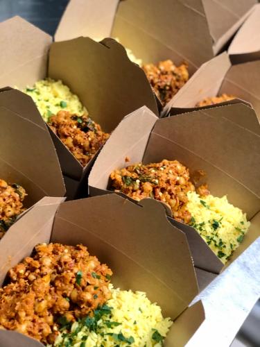 Shot of several takeaway boxes filled with a moroccan chickpea tagine and cauliflower rice. 