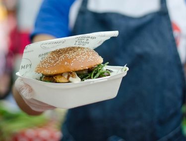 Close up of a hand presenting a burger in a burger box with Shrimpy's food wrap — a London food stall