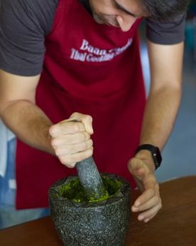 Man using a mortal and pestle to grind fresh herbs and spices