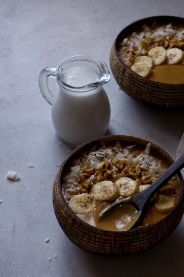 Two smoothie bowls next to a jug of coconut milk 