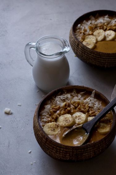 Two smoothie bowls next to a jug of coconut milk