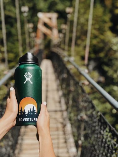 Hands holding a stainless steel bottle on a bridge in the forest