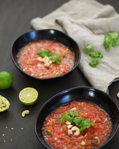 90 degree angle shot of two bowls filled with watermelon gazpacho, garnished with roasted cashews and coriander on a table with a linen cloth and lime halves