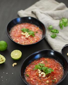 90 degree angle shot of two bowls filled with watermelon gazpacho, garnished with roasted cashews and coriander on a table with a linen cloth and lime halves