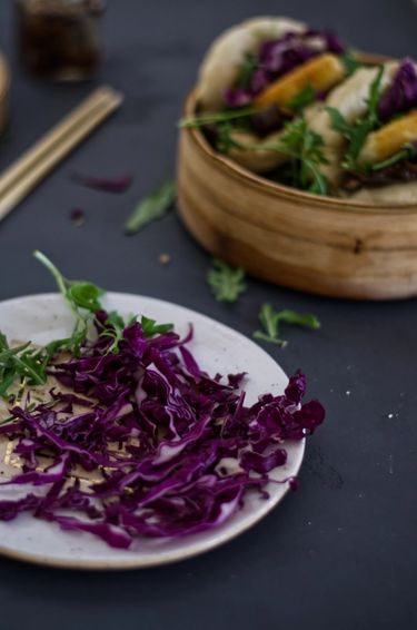 Plate with fresh cabbage and rocket, next to a steamer with bao buns (gua bao) with rocket, cabbage, and fried goats cheese