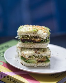 Two square sandwiches stacked on a plate, placed on a book