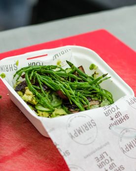 Picture of a burger topped with samphire from a London based food stall specialising in shrimp burgers, preparing a shrimp burger at their food stall in Broadway Market