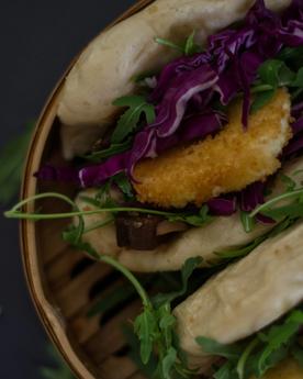 Close up shot of bao buns (gua bao) with rocket, cabbage, and fried goats cheese in a bamboo steamer