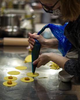 Woman piping a pumpkin filling into fresh ravioli in an industrial kitchen