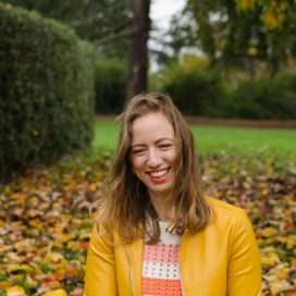 A smiling woman sitting on a bed of autumn leaves at Kew Gardens London