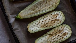 Four halves of raw aubergine on a baking tray