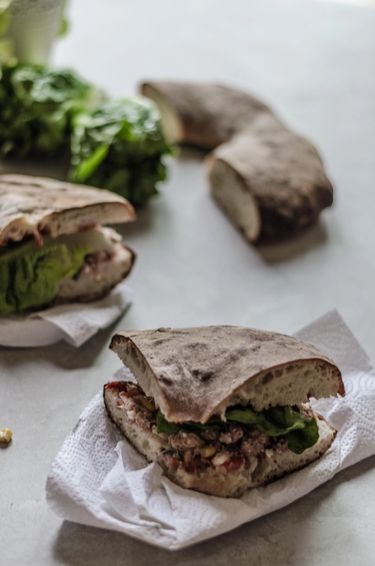 Several slices of Maltese ftira bread or hobz biz-zejt — a sandwich stuffed with tuna, capers, olives, goats cheese, lettuce, pickled vegetables and more.