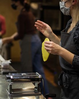 Woman holding a rolled out dough above a pasta machine, in a cooking class.