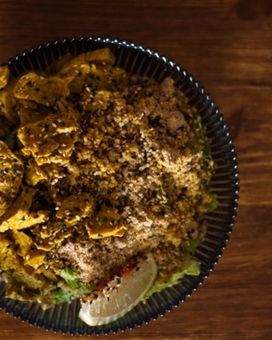 Overhead shot of a bowl of seitan curry with rice and wedge of lime sitting atop a bench