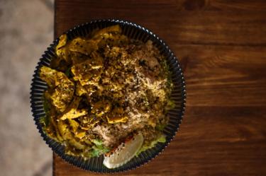 Overhead shot of a bowl of seitan curry with rice and wedge of lime sitting atop a bench