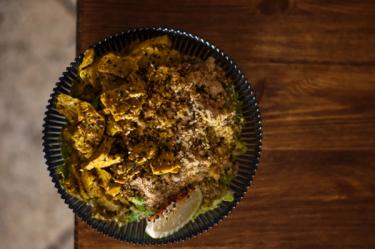 Overhead shot of a bowl of seitan curry with rice and wedge of lime sitting atop a bench 