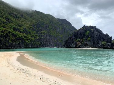 Rugged jungle cliffs and a pristine sandy beach with turquoise waters in the Philippines