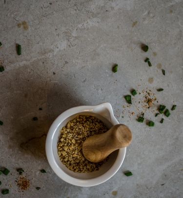 Bowl with dukkah (crushed nuts and seeds) on a surface sprinkled with chopped scallions