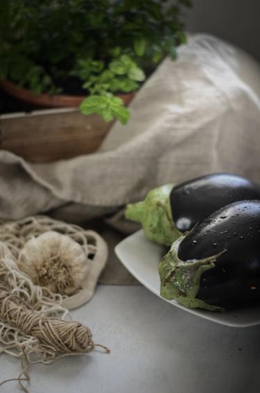 Two aubergines in a plate surrounded by items on a table 