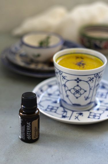 Turmeric milk in a bone china tea cup and saucer with a bottle of ginger essential oil next to it