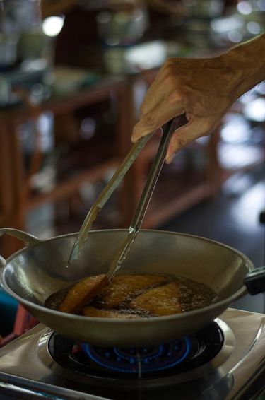 Hand holding tongs whilst frying toast in a wok