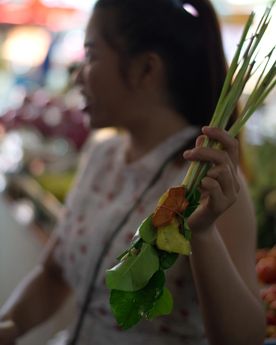 Girl holding out a bunch of leaves from an Asian wet market