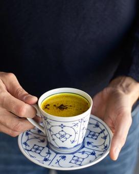 Man holding turmeric milk in a bone china tea cup and saucer