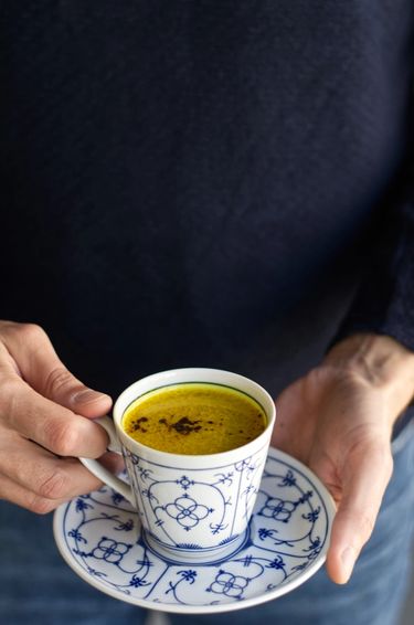 Man holding turmeric milk in a bone china tea cup and saucer