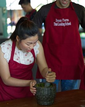 Photo of an Asia chef mashing herbs in a mortar and pestle with a student observing