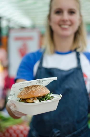 Picture of founder of Shrimpy, a London based food stall specialising in shrimp burgers, handing out a shrimp burger at their food stall in Broadway Market