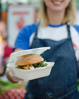 Picture of founder of Shrimpy, a London based food stall specialising in shrimp burgers, handing out a shrimp burger at their food stall in Broadway Market