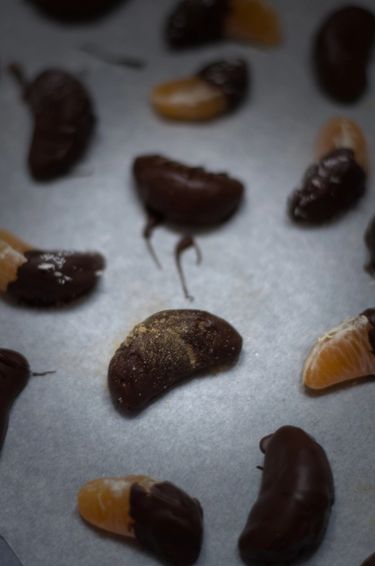 Several clementine segments coated in chocolate on baking paper