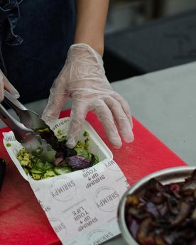 Picture of founder of Shrimpy, a London based food stall specialising in shrimp burgers, preparing a shrimp burger at their food stall in Broadway Market