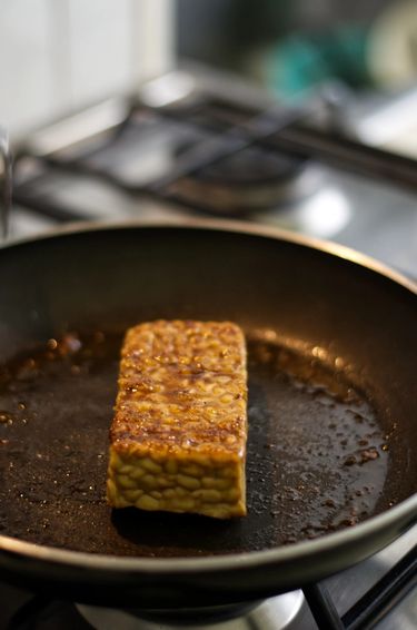 Pan fried tempeh in a pan on a stove