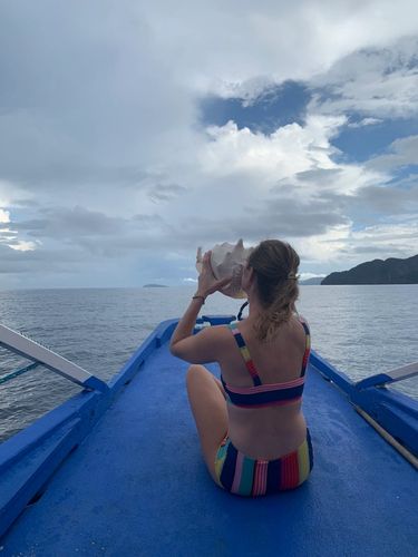 Girl at the edge of a boat holding a cone shell to her mouth