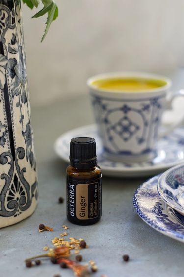 Turmeric milk in a bone china tea cup and saucer on a surface with some dried chilies and a bottle of ginger essential oil